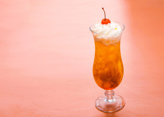 Glass of cocktail decorated with whipped cream and red cherry on pink table