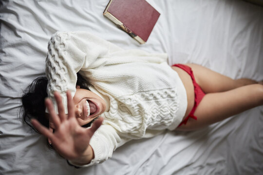 Young Latin woman laying on the bed happily smiling with her face covered