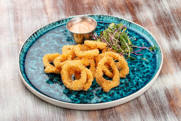 Squid rings fried in batter with sauce on a decorative plate