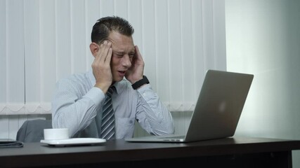 A business man who is a company employee using a laptop to work in an office feel so stressed that they have a headache from long, hard work.