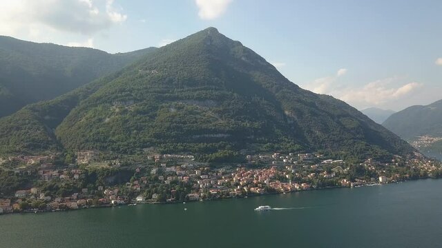 A large green mountain next to a lake with a big boat driving by in Italy, Como lake