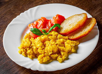 Scrambled eggs with smoked salmon and toast in white plate on wooden table background