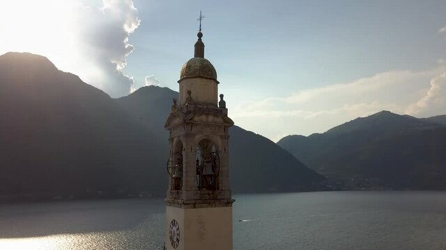 Church clock tower at the beautiful Como lake and mountains in the background with sunshine in Nesso, Italy