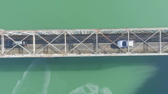 Two cars driving through narrow metal baltimore type bridge on lake, overhead static aerial
