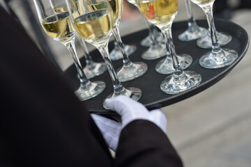 A waiter's hand wearing a white glove holding a a bunch of Champagne glasses on a plate 