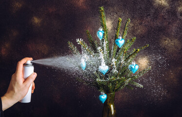 Close up view of person hand using canned spray snow to spray decorate Christmas tree branches in...