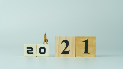 Miniature people businessman in brown suit with Briefcase Bag stand on wooden number 2021.Moving into 2021 concept