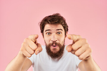 Bearded man in white t-shirt gesturing with hands facial expression close up pink background
