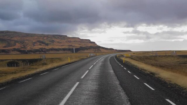 View from inside car or van on empty hilly road leading to horizon line, endless travelling roadtrip destination.Cloudy sunset view of 1 main road in Iceland through car window.