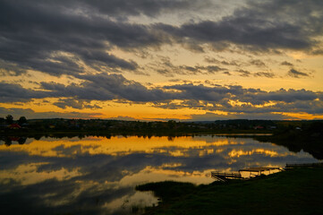 Summer sunset over lake near small town. Sky with clouds