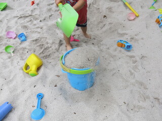 the child in red having lots of fun in the white sandpit with a green shovel