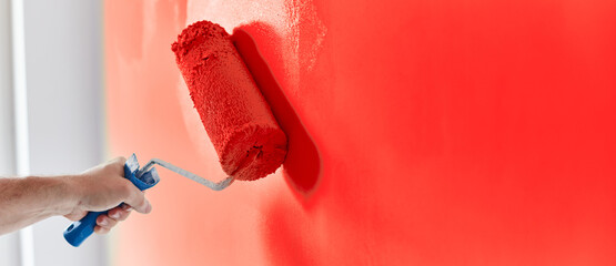 Male hand painting wall with paint roller. Painting apartment, renovating with red color paint
