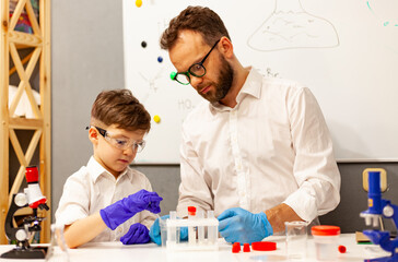 dad and son the child stayed at home conduct experiments on a white table, behind them on the wall is a white Board magnetic-marker