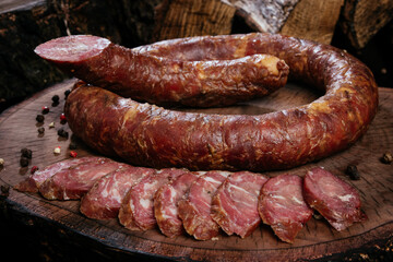 Whole fresh smoked sausage on a dark wooden stump background, circle and slices