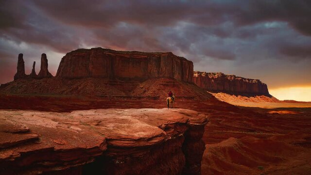 Cinemagraph / seamless video loop time-lapse of a Navajo Native American on a horse looking over the famous rock formations at Monument Valley landmark in Utah / Arizona, America / USA while sunset.