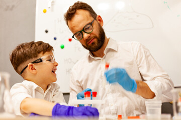 dad and son the child stayed at home conduct experiments on a white table, behind them on the wall is a white Board magnetic-marker