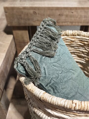 Fototapeta premium Basic vintage pale green cotton cushion with fringes in a wicker basket. Ethnic and hygge interior decoration. Corner detail of natural pillow with beaded fringe.