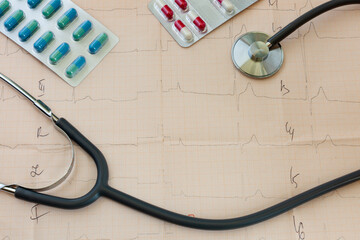 medical statoscope and tablets of different colors in blisters on a table with a cardiologist lies on a cardiogram