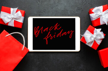 Black Friday - red handwriting on the tablet screen. Gift boxes with ribbons. The concept of holiday sales