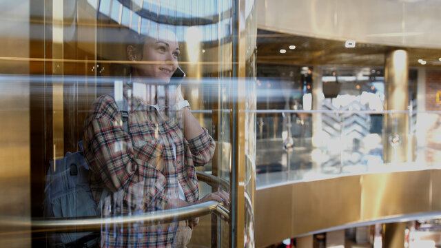 Attractive brunette business lady in modern steel elevator in large office center and talking on cell phone. Young businesswoman talks by smartphone and leaves elevator