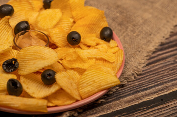 Crispy, delicious potato chips with mustard sauce and olives on a coarse homespun cloth. Close up.