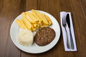 Tasty combination of hamburger accompanied by rice and fries. fork and knife on the right side of the plate.