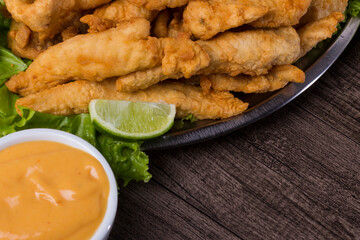 Fried fish served on lettuce leaves with lemons and tartar sauce to accompany. Close-up photograph with lower right space for texts.