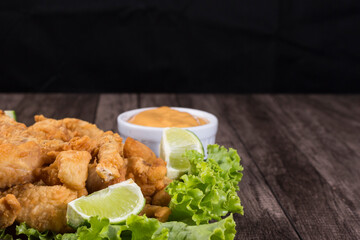 Portion and fried fish served on lettuce leaves with lemons and sauce to accompany. Close-up photograph with upper space for texts.