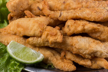 Portion and fried fish served on lettuce leaves with lemon to accompany. Gastronomic photography close up.