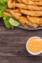 Fried fish served on lettuce leaves with lemons and tartar sauce to accompany. Vertical gastronomic photography. Served in the best restaurants.