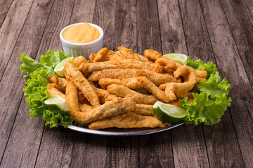 Gourmet photograph of portion and breaded fried fish served on lettuce leaves with lemons and...