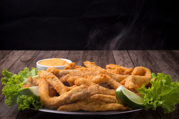 Breaded fried fish served on lettuce leaves with lemons and tartar sauce to accompany. Hot with smoke. Close-up photography.