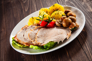 Roasted pork ham, champignons and boiled potatoes on wooden table
