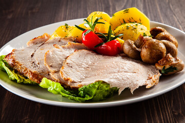 Roasted pork ham, champignons and boiled potatoes on wooden table
