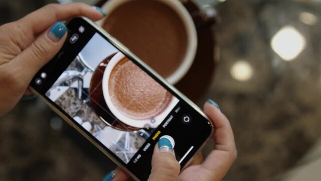 Close up of woman holds modern smartphone and taking pictures of cocoa to share photos on social media resources