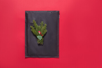 Black bubble envelope decorated with christmas tree ornament on red background