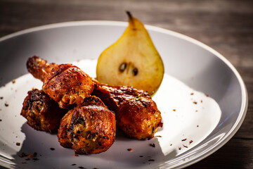 Barbecue chicken drumsticks with fried pear on wooden table
