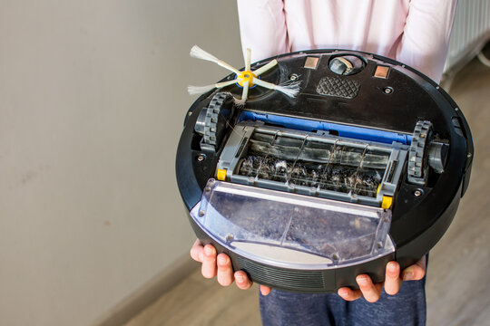 Robotic vacuum clener upside down with dust, trash and hair in human hands. Smart cleaning concept.