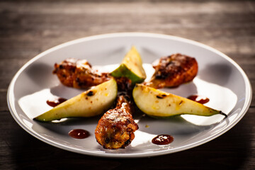 Barbecue chicken drumsticks with fried pear on wooden table

