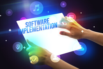 Holding futuristic tablet with SOFTWARE IMPLEMENTATION inscription, new technology concept