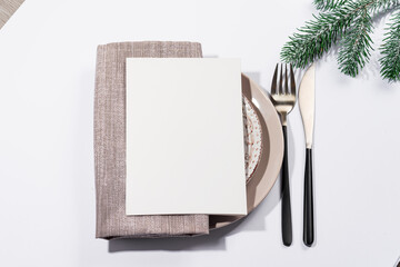 Winter festive table setting with cutlery and white brochure on table. Christmas tableware.