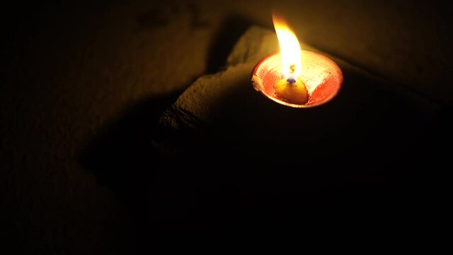 dark minimalistic image showing a diya oil lamp filled with oil or ghee and burning a cotton wick to produce a flame, its a popular religious item and decoration item on the hindu festival of diwali. 