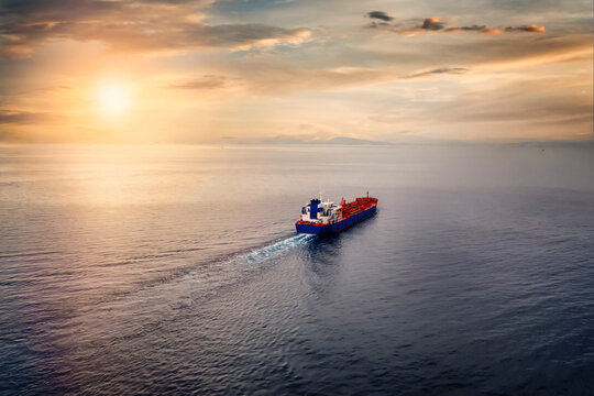 Aerial view of a container cargo ship sailing over calm sea into the sunset