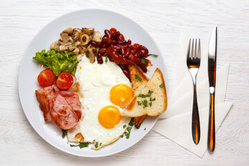 English Breakfast, fried eggs, ham, mushrooms on a white plate with a knife and fork