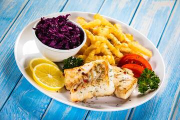 Fish dish - fried cod fillet with curly french fries and vegetable salad on wooden table
