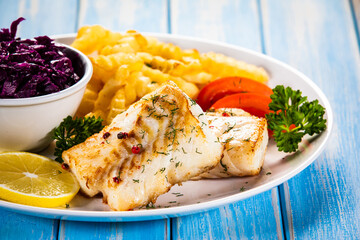 Fish dish - fried cod fillet with curly french fries and vegetable salad on wooden table
