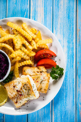 Fish dish - fried cod fillet with curly french fries and vegetable salad on wooden table
