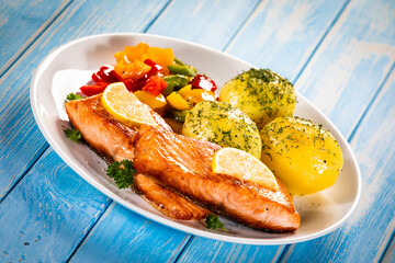 Fried salmon steaks with lemon, boiled potatoes and bell pepper served on wooden table