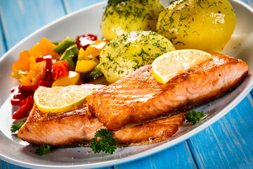 Fried salmon steaks with lemon, boiled potatoes and bell pepper served on wooden table