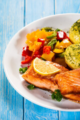 Fried salmon steaks with lemon, boiled potatoes and bell pepper served on wooden table
